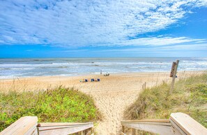 Een strand met een houten vogelbeschermingsgang naar het water, een bord en strandstoelen.