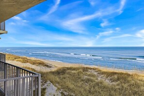 Une vue sur la plage, avec une balustrade en bois et des dunes herbeuses.