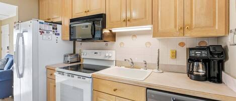 A compact kitchen with wooden cabinets, a microwave, a toaster, an oven, a sink, a coffee maker, and a dishwasher.