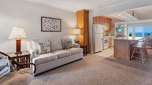 Een moderne keuken met een centraal eiland, een eethoek met barstoelen, en een woonkamer met een bank en decoratieve kussens.
