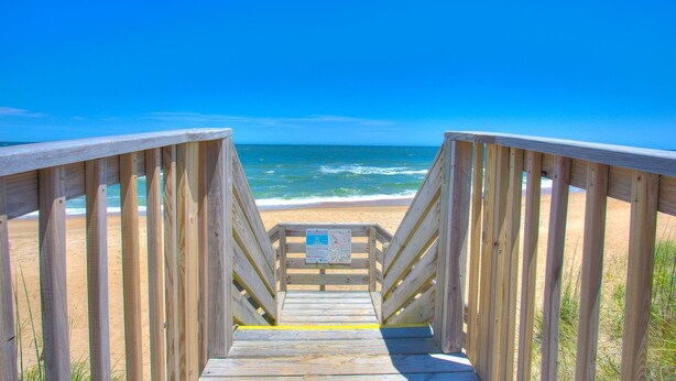 A wooden boardwalk leading to a beach with clear blue skies. - Cozy 3-Bedroom Retreat in Duck – Walk to Beach! (Duck)