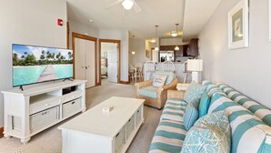 A living room with a television, a white coffee table, a striped sofa, wicker chairs, and a ceiling fan.