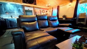 A cozy living room with a sectional sofa, a wooden coffee table, and a kitchen area in the background. - Wolf's Cabin Near Historic Downtown Noblesville (Noblesville)
