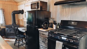 A compact kitchen with a stove, microwave, refrigerator, and a wood stove. - Wolf's Cabin Near Historic Downtown Noblesville (Noblesville)