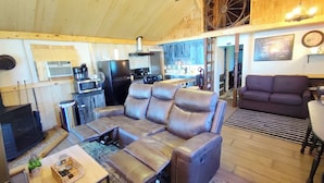 A cozy living room with a sectional sofa, a flat-screen TV, and a kitchen area with a stove and refrigerator. - Wolf's Cabin Near Historic Downtown Noblesville (Noblesville)