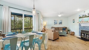 A dining area with a table and chairs, a sofa, and a fireplace. - Cozy 2BR Retreat | Pool, Tennis & Quick Beach Access (Kill Devil Hills)