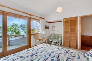 Une chambre avec une grande fenêtre, un lit recouvert d’une couette à motifs, une chaise, un canapé et une armoire en bois.