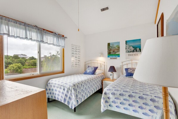 Une chambre avec deux lits simples, un bureau et une fenêtre donnant sur des maisons et de la verdure.