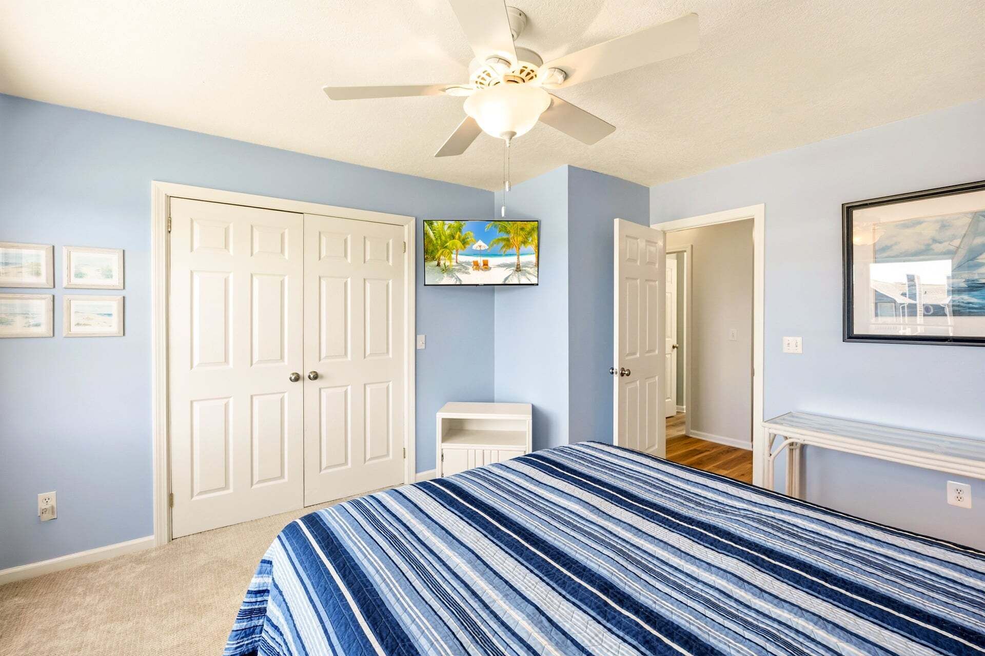 A bedroom with a bed, a ceiling fan, a door, and a framed picture on the wall.