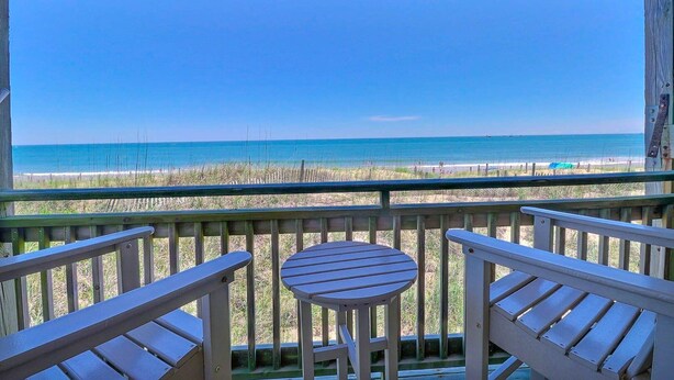 A wooden deck with a table and chairs overlooking a beach.