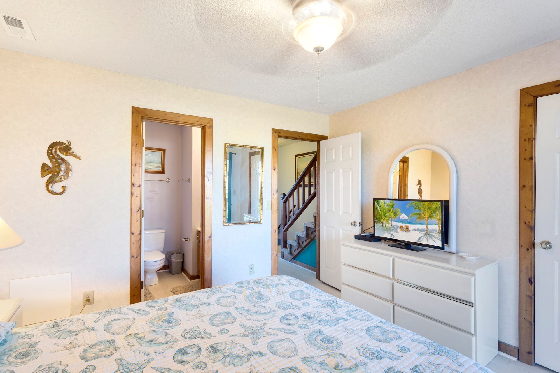 A bedroom with a bed, a dresser, a mirror, and a door leading to a bathroom.