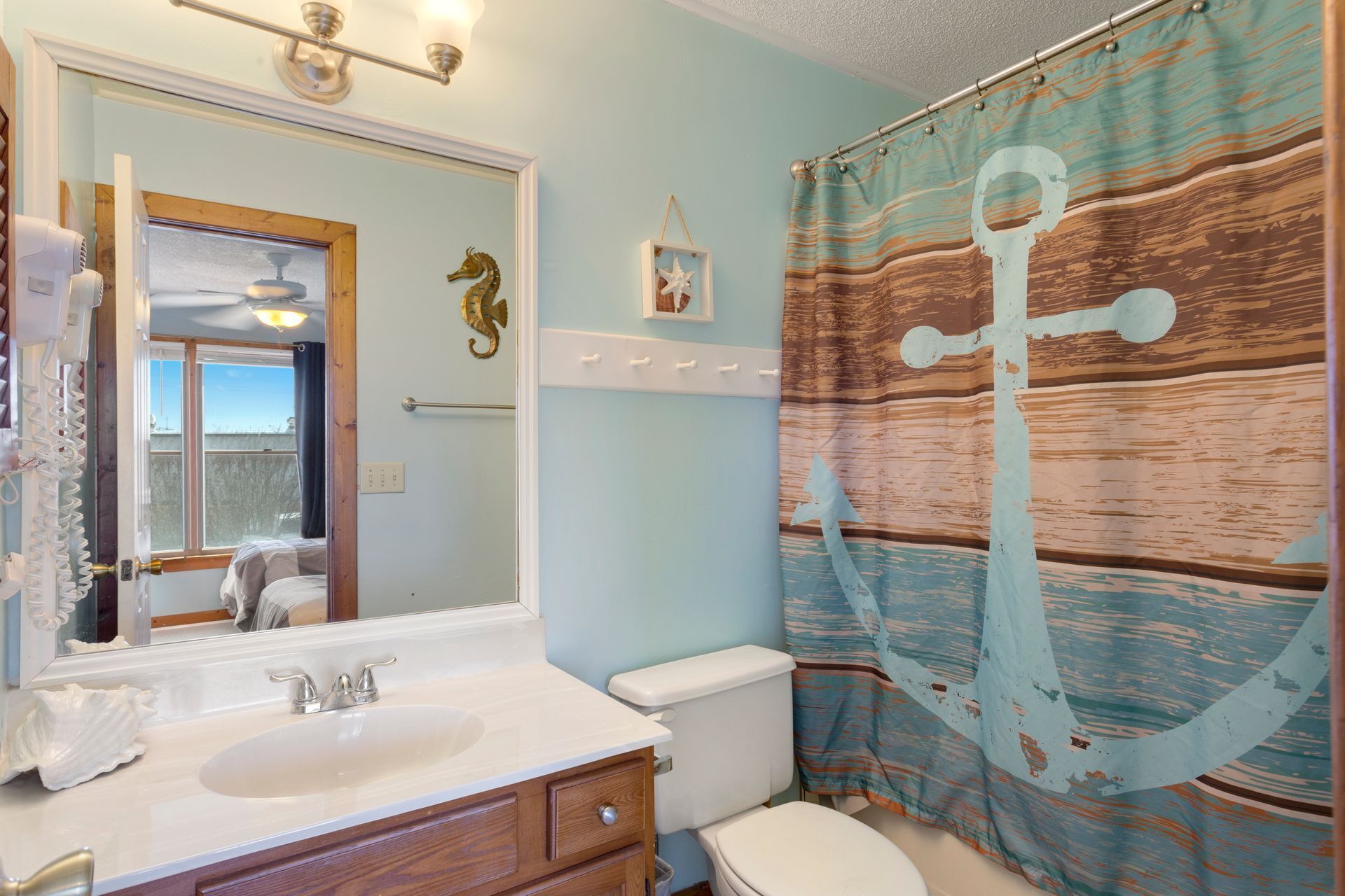 A bathroom with a sink, mirror, toilet, and a shower curtain with an anchor design.