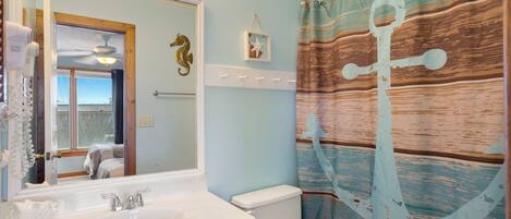 A bathroom with a sink, mirror, toilet, and a shower curtain with an anchor design.
