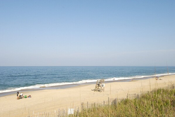 A beach with a sandy shore, a wooden lifeguard stand, and a few people in the distance. - SW11 A Great Escape * Oceanfront * Community Pool (Kill Devil Hills)