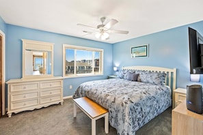 Une chambre à coucher comprenant un lit, un ventilateur de plafond, une fenêtre, une commode, un banc et un téléviseur.