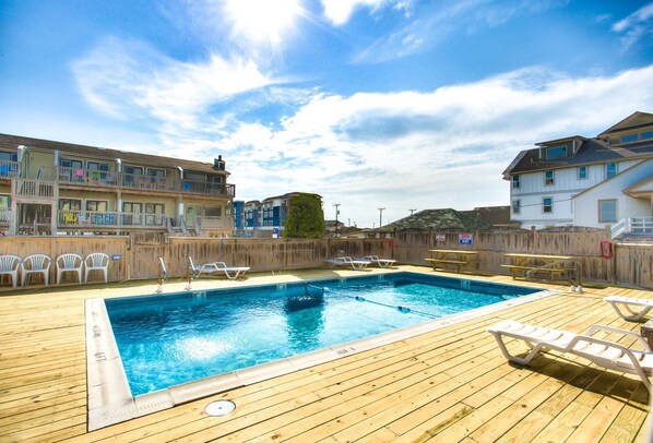 Une piscine avec une terrasse en bois, des chaises longues et une clôture en bois.
