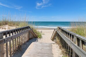 Walk along the weathered boardwalk to the shoreline, surrounded by tall grasses and sand dunes.