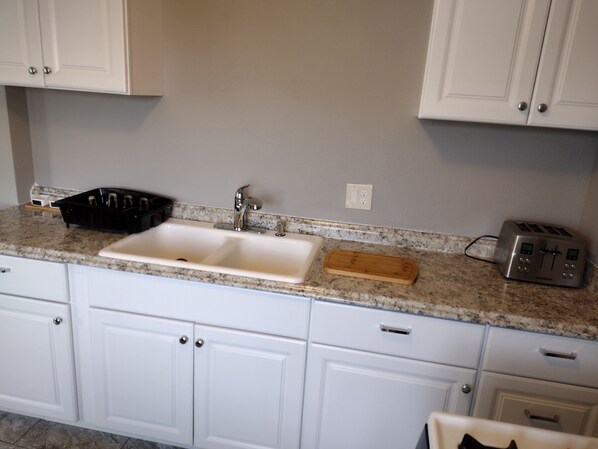 A kitchen with white cabinets, a double sink, a toaster, and a wooden cutting board on the countertop. - Room With Views of Beautiful Taylor Mountain (Santa Rosa)