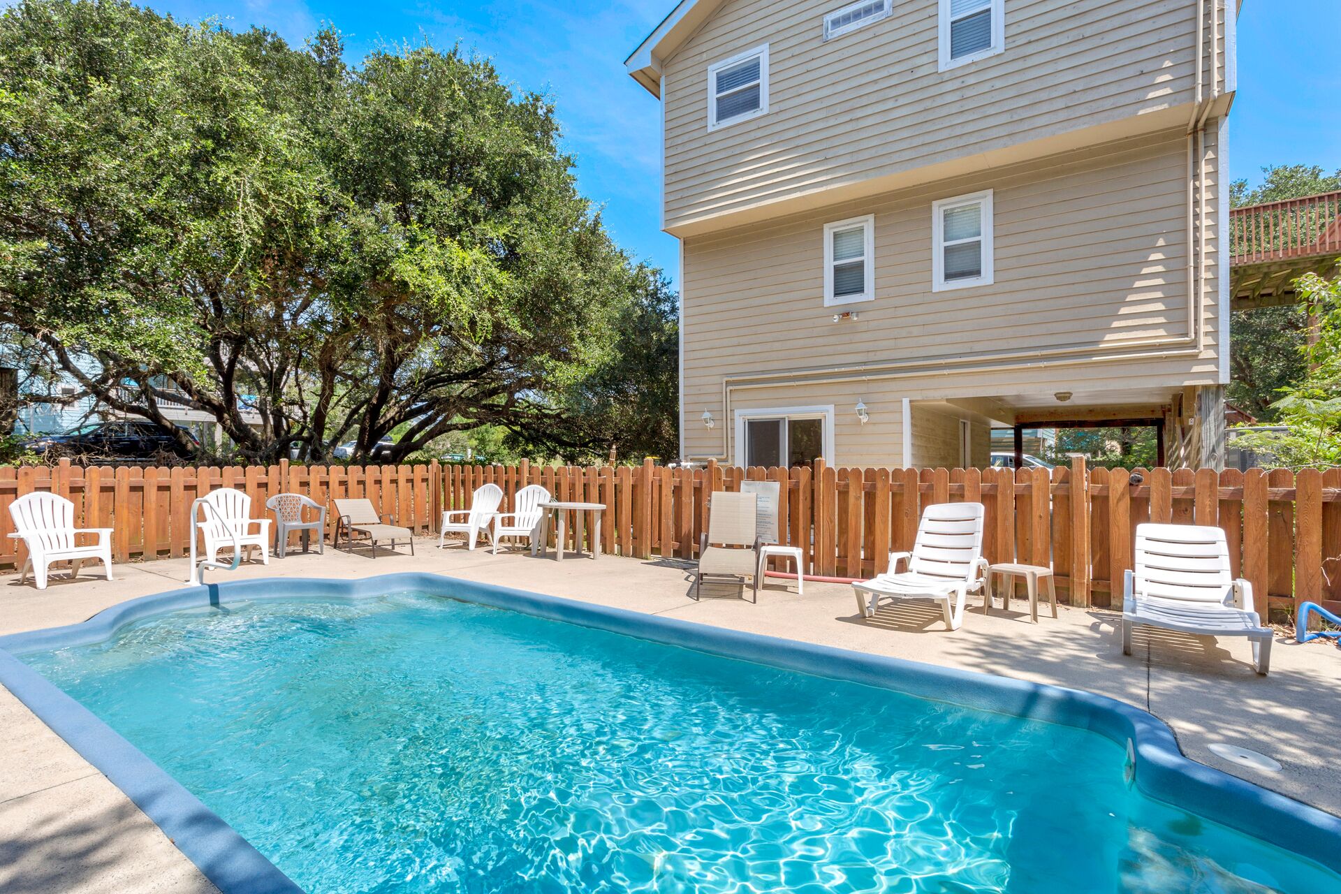 A swimming pool with lounge chairs and a wooden fence.