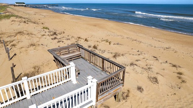 A beach with a wooden deck and a pier in the background.