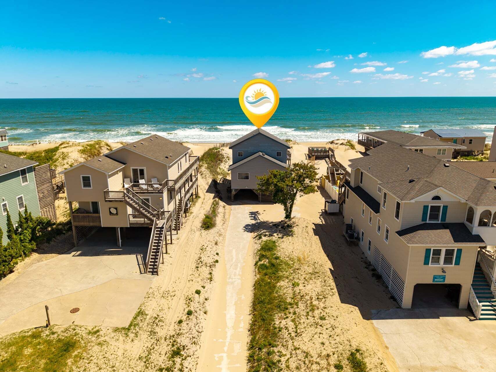A beachfront residential area with houses, a sandy path, and the ocean in the background.