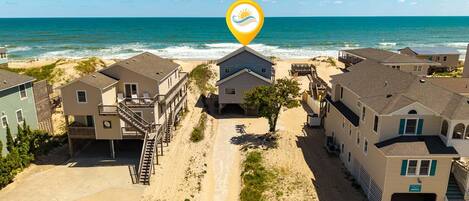A beachfront residential area with houses, a sandy path, and the ocean in the background.
