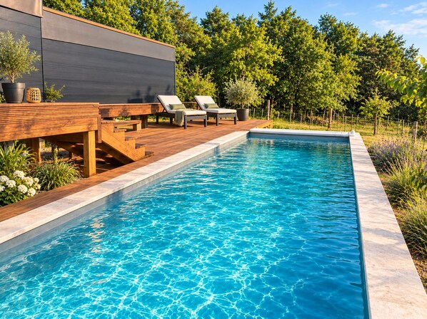 A rectangular swimming pool with clear blue water, surrounded by a wooden deck and lounge chairs. - Maison en pleine nature (Valencisse)