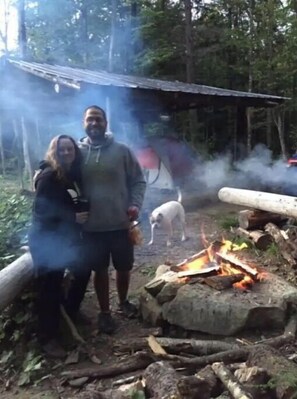Enjoy a campfire in a serene wooded area, surrounded by nature and a rustic cabin.