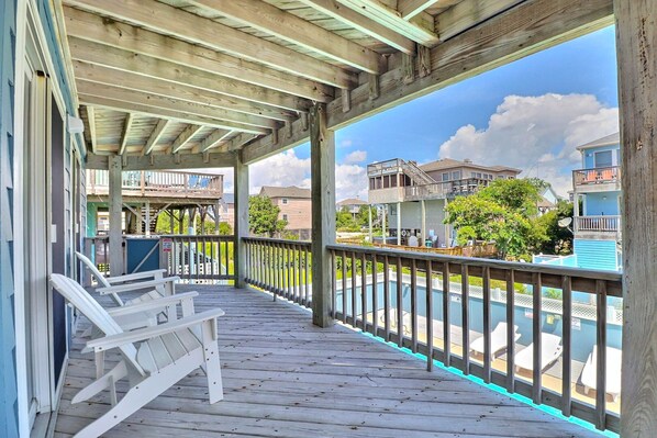 A wooden deck with a view of a swimming pool and neighboring houses. - Sea Nest – Beach, Pool, Hot Tub & Pets (Corolla)