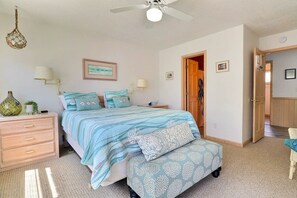 A bedroom with a bed, bedside tables, a hanging light fixture, and a door leading to another room.