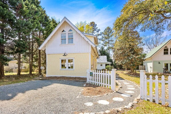 A two-story house with a white picket fence, a gravel driveway, and a small garden area.