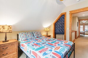 A bedroom with a bed, two nightstands, a wooden dresser, and a staircase leading to another room.