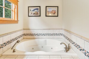 A bathroom with a large bathtub, tiled walls, and two framed pictures on the wall.