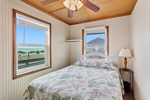 Une chambre à coucher avec un lit, un ventilateur de plafond, une fenêtre donnant sur la plage et une lampe sur une table de chevet.