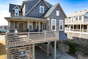 A beachfront house with a covered porch, a deck, and a staircase leading to a second floor.