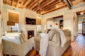 A spacious living room with a fireplace, comfortable seating, and a kitchen area visible through an open doorway.
