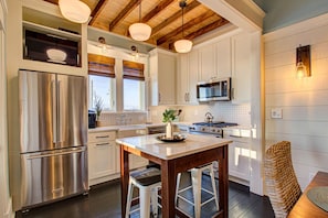 A modern kitchen with stainless steel appliances, a wooden ceiling, and a central island with bar stools.