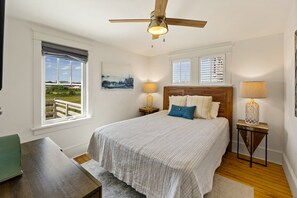 A bedroom with a bed, two bedside tables, a ceiling fan, and two windows with blinds.