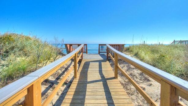 Un paseo marítimo de madera que conduce a una playa con cielos despejados.