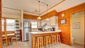Una cocina con paredes de madera, un refrigerador de acero inoxidable, un microondas y un fregadero. Hay taburetes de madera en la barra.