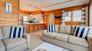 Interior acogedor de una cabaña con detalles de madera, una kitchenette, un comedor y una sala de estar con sofá y sillones.