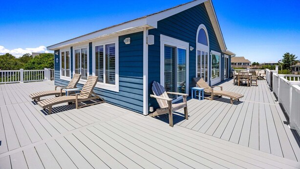 A blue building with white trim, a deck with wooden chairs and tables, and a clear blue sky. - La Ballena Cottage Dog Friendly Pool Ocean Views (Corolla)