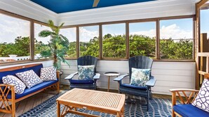 A sunroom with a ceiling fan, large windows, a wooden table, blue and white patterned furniture, and a potted plant. - La Ballena Cottage Dog Friendly Pool Ocean Views (Corolla)