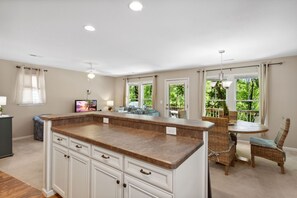 A spacious kitchen with a central island, large windows, and a dining area with wicker furniture.