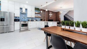 A modern kitchen with white cabinets, a wooden dining table, and a built-in stove. - Home 4 King Beds - Large Garage by StayStLouis (St. Louis)