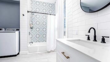 Ein modernes Badezimmer mit einem weißen Waschbecken, einem schwarzen Wasserhahn und einer Dusche mit gemusterten Fliesen.