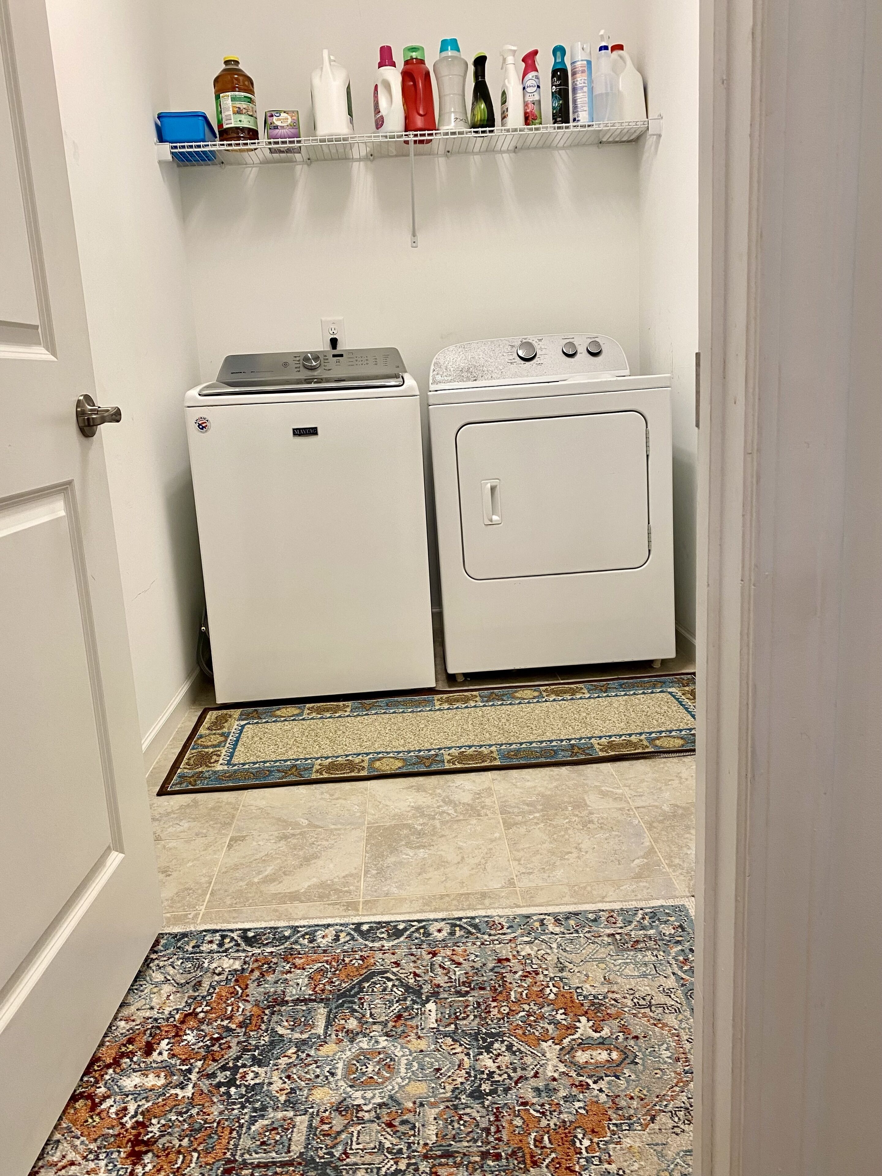 A laundry area with a washing machine and dryer, a shelf with cleaning supplies, and a patterned rug.