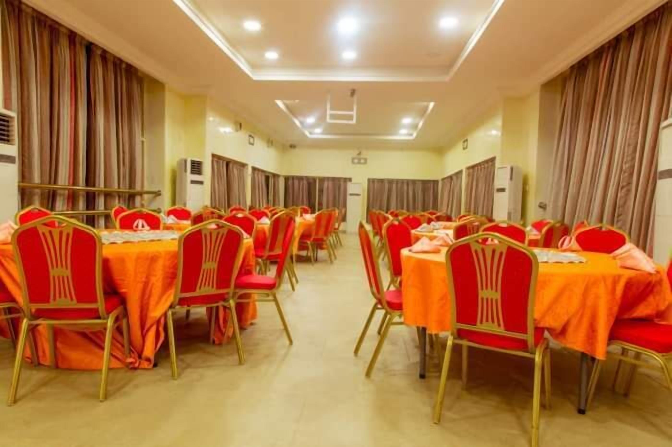 A conference room with rows of tables and chairs, air conditioning units, and curtains.