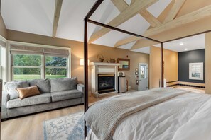A bedroom with a large bed, a sofa, a fireplace, and a view of the outdoors.
