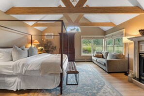 A bedroom with a four-poster bed, a bench, a sofa, and a fireplace.